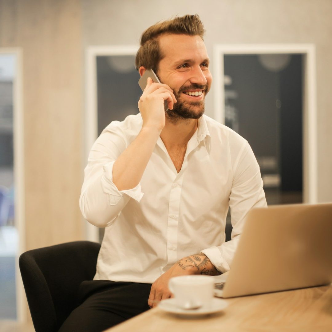 Mann telefoniert / Recruiting Beratung: Recruiting-Beratung für Unternehmen: Mann im weißen Hemd sitzt am Tisch und telefoniert